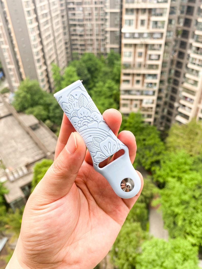 May include: A light blue silicone watch band with a white floral pattern. The band has a silver metal connector.