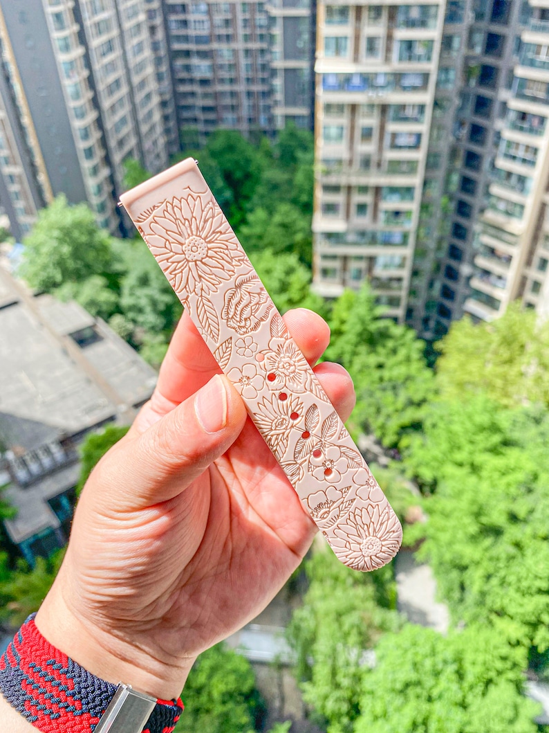 May include: A pale pink watch band with a floral pattern. The band is made of silicone and has a textured surface.