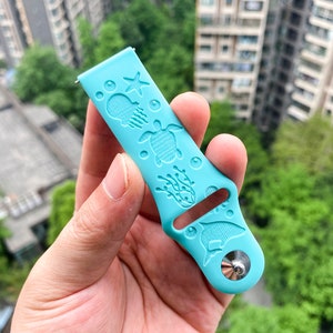 以下が含まれることがあります： 海をテーマにしたデザインの薄い青色のシリコン製腕時計バンド。バンドには、ヒトデ、クラゲ、ウミガメ、海藻、イルカが描かれています。バンドには銀色の金属製のバックルが付いています。
