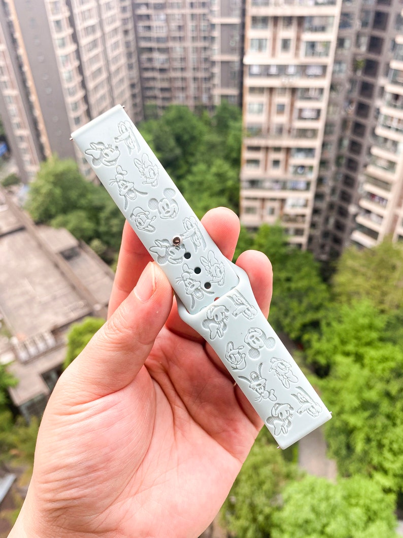 May include: A light blue silicone watch strap with a white Mickey Mouse design.
