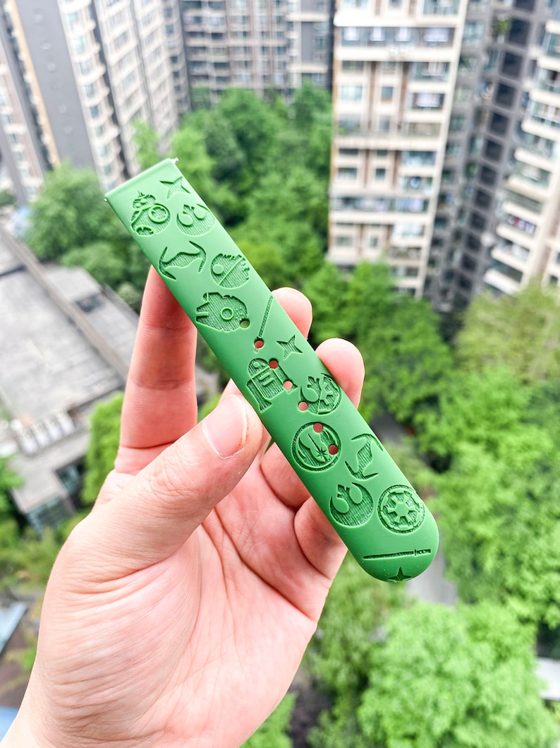 May include: Green watch strap featuring a Star Wars theme. The strap is embossed with various Star Wars characters and symbols, including the Death Star, R2-D2, and the Millennium Falcon.