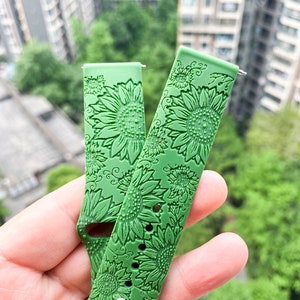 May include: Two green silicone watch bands with a sunflower pattern. The bands are designed for smartwatches.