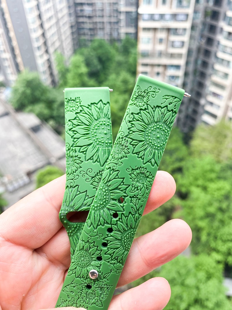 May include: Two green silicone watch bands with a sunflower pattern. The bands are designed for smartwatches.