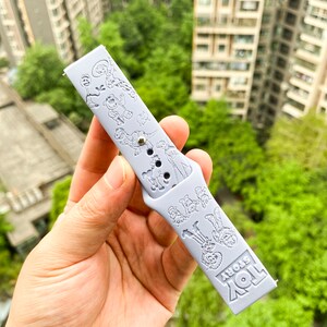 以下が含まれることがあります： おもちゃの物語のキャラクターが白くエンボス加工された、薄い青色のシリコン製腕時計バンド。バンドには「トイストーリー」の文字が印刷されています。