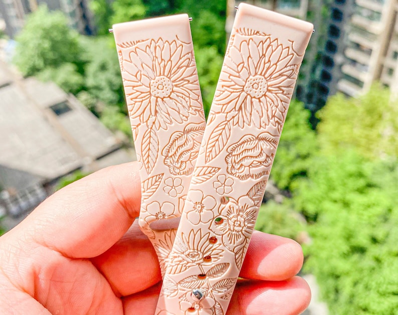 May include: Two pink silicone watch bands with a floral pattern. The bands have a raised design of flowers and leaves.