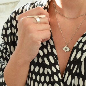 May include: A silver necklace with a white eye pendant on a black and white polka dot shirt.