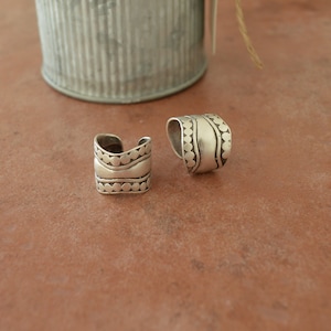 May include: Two silver rings with a textured design. The rings are made of metal and have a rounded shape.