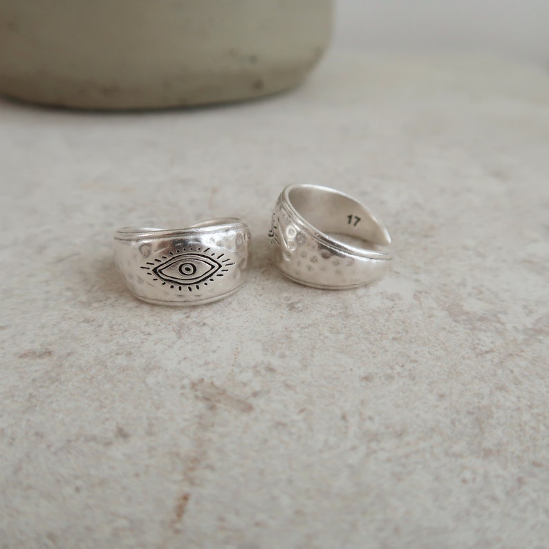 Peut inclure: Deux bagues argent&eacute;es &agrave; la texture martel&eacute;e. L'une des bagues pr&eacute;sente un symbole d'&oelig;il grav&eacute; en noir avec des lignes rayonnantes. L'autre bague est ouverte et affiche le nombre 17 grav&eacute; sur la surface int&eacute;rieure de l'anneau.