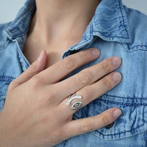 May include: A silver ring with an eye design. The ring is open and adjustable. The eye is detailed with a black pupil and white sclera.