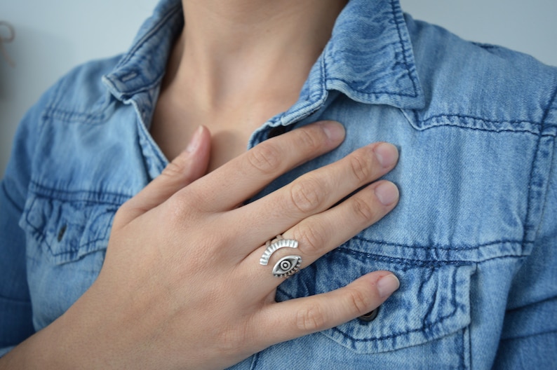 May include: A silver ring with an eye design. The ring is open and adjustable. The eye is detailed with a black pupil and white sclera.