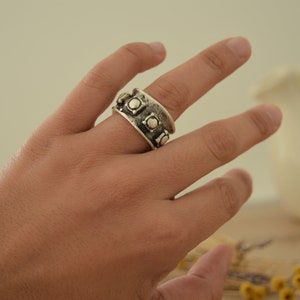 May include: A silver ring with a textured band and round, raised accents.