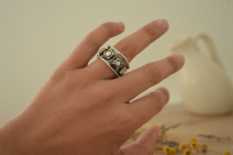 May include: A silver ring with a textured band and round, raised accents.