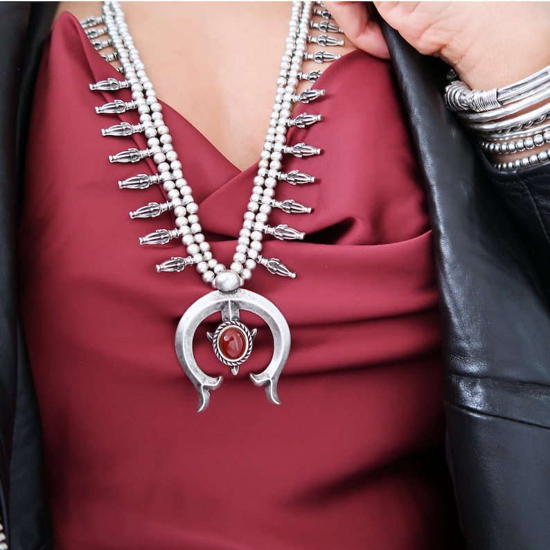 May include: A silver necklace with a large, ornate pendant featuring a red gemstone. The necklace is layered and has a southwestern style.