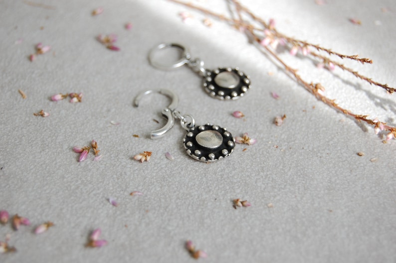 May include: A pair of silver hoop earrings with a round, textured silver charm hanging from each hoop.