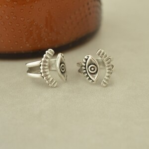 May include: Two silver toe rings with an eye design. The rings are open and adjustable.