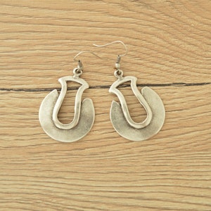 May include: A pair of silver hoop earrings with a unique, abstract design. The earrings are made of metal and have a slightly oxidized finish.