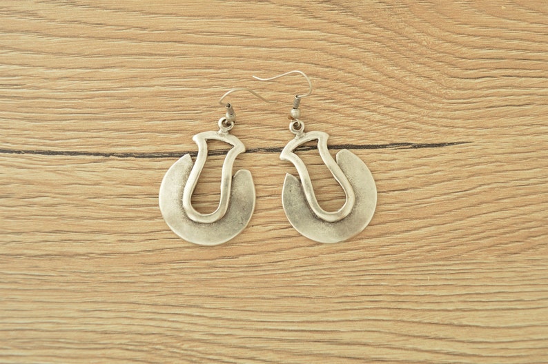 May include: A pair of silver hoop earrings with a unique, abstract design. The earrings are made of metal and have a slightly oxidized finish.