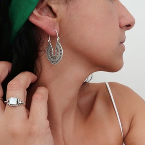 Puede incluir: Pendientes plateados, de dise&ntilde;o intrincado con forma de l&aacute;grima. Los pendientes presentan un patr&oacute;n calado detallado. Tambi&eacute;n se ve un anillo plateado con una piedra blanca cuadrada. La imagen muestra joyas.