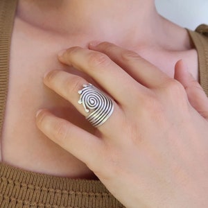 Op de afbeelding: Een zilveren ring met een spiraalvormig ontwerp. De ring is verstelbaar en kan aan elke vinger worden gedragen.