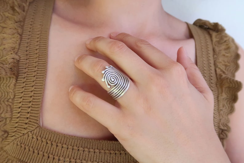 Op de afbeelding: Een zilveren ring met een spiraalvormig ontwerp. De ring is verstelbaar en kan aan elke vinger worden gedragen.