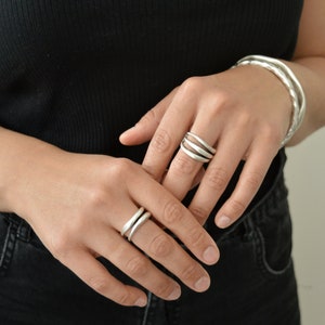Puede incluir: Dos anillos de plata con un diseño ondulado. Los anillos se llevan en los dedos de la mano de una persona.