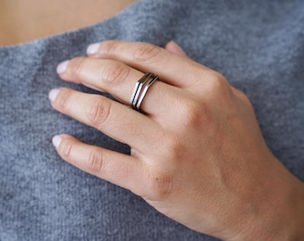 May include: A silver ring with three stacked bands, each with a slightly different shape.