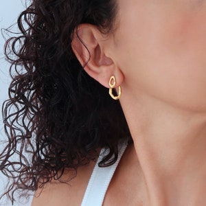 Puede incluir: Pendientes de aro abiertos texturizados de color dorado. Los pendientes los lleva una persona con el pelo rizado.