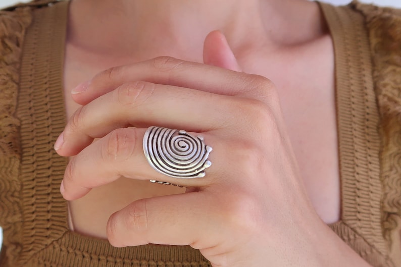 Op de afbeelding: Een zilveren ring met een spiraalvormig ontwerp. De ring wordt aan een vinger gedragen.