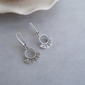 May include: A pair of silver earrings with a circular design and a textured fan-shaped detail.