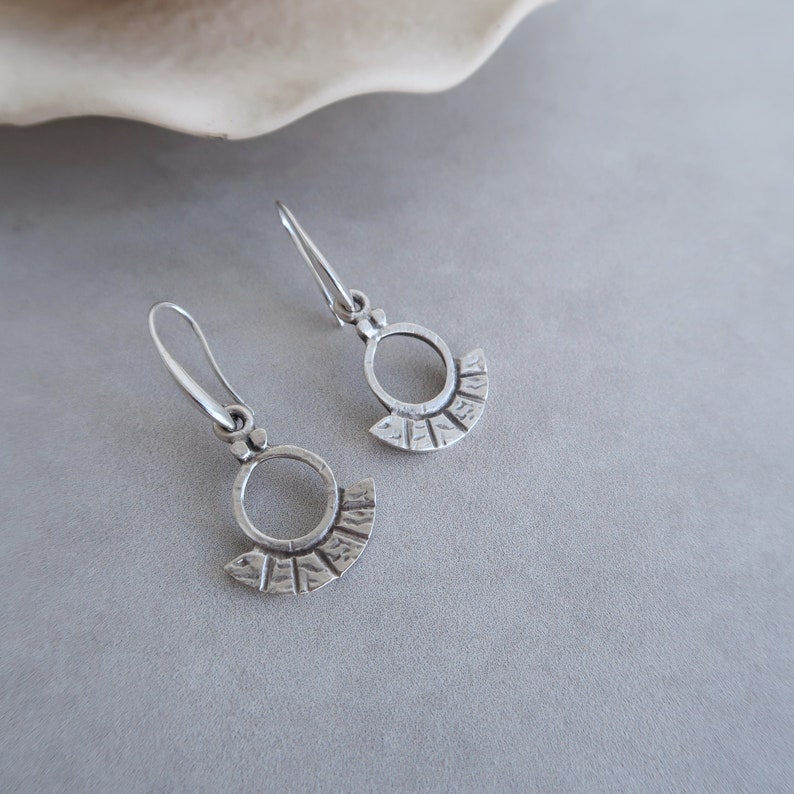 May include: A pair of silver earrings with a circular design and a textured fan-shaped detail.