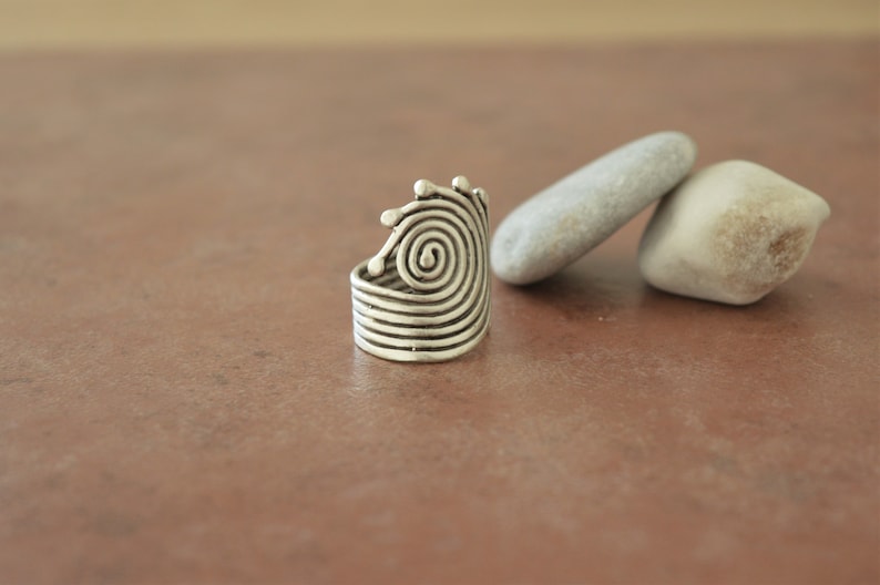 Op de afbeelding: Een zilveren ring met een spiraalvormig ontwerp. De ring is gemaakt van metaal en heeft een getextureerd oppervlak.