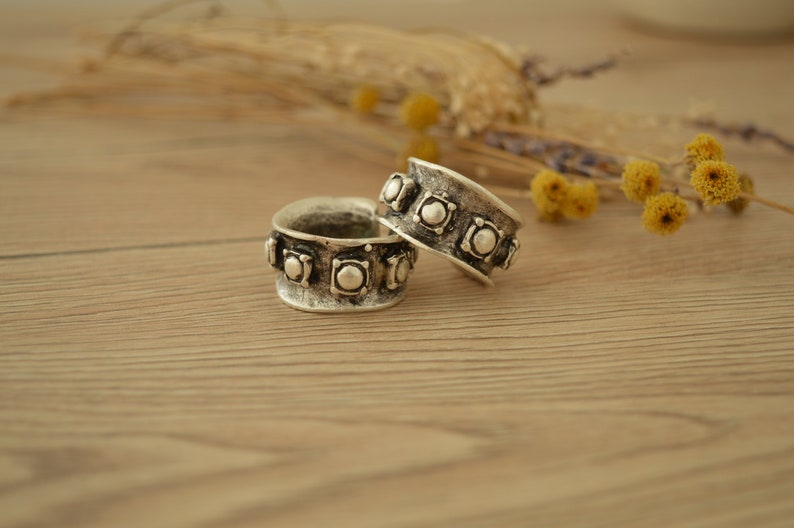 May include: Two silver rings with a decorative design of raised circles. The rings are on a wooden surface.