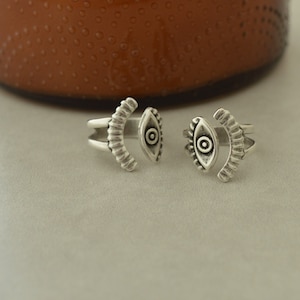 May include: Two silver rings with an eye design. The rings are open and adjustable.