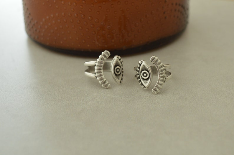 May include: Two silver rings with an eye design. The rings are open and adjustable.