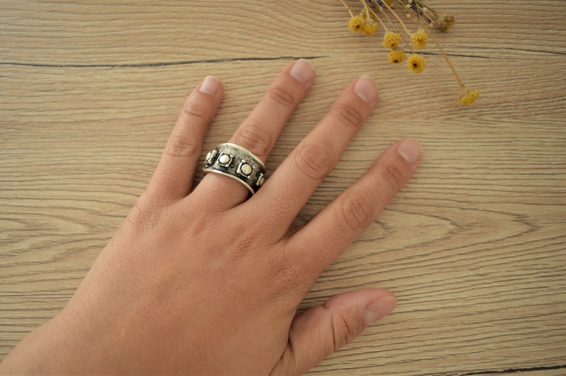 May include: A silver ring with a textured band and round silver accents. The ring is worn on a person's finger.