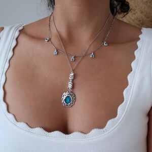 May include: A silver necklace with a turquoise pendant and smaller turquoise stones hanging from the chain. The pendant is a circle with a smaller circle in the centre.