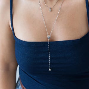 May include: A layered necklace set featuring three necklaces. The top necklace has small, colourful beads. The middle necklace has a small pendant. The longest necklace is silver with a decorative pendant and a dangling bead.