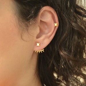 May include: Gold ear cuff earrings with a star design and a row of small spikes. The earrings are worn in the upper ear lobe and helix piercing.