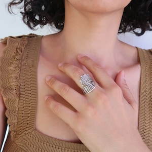 Op de afbeelding: Een zilveren ring met een spiraalvormig ontwerp. De ring wordt gedragen aan de wijsvinger van een hand.
