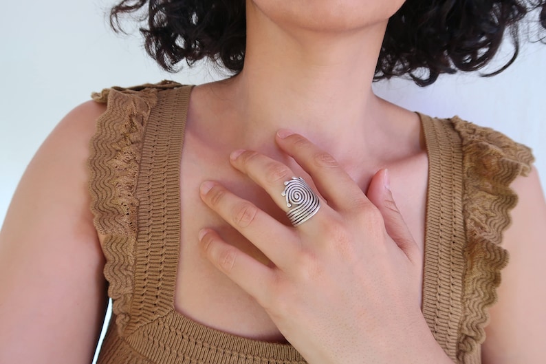 Op de afbeelding: Een zilveren ring met een spiraalvormig ontwerp. De ring wordt gedragen aan de wijsvinger van een hand.