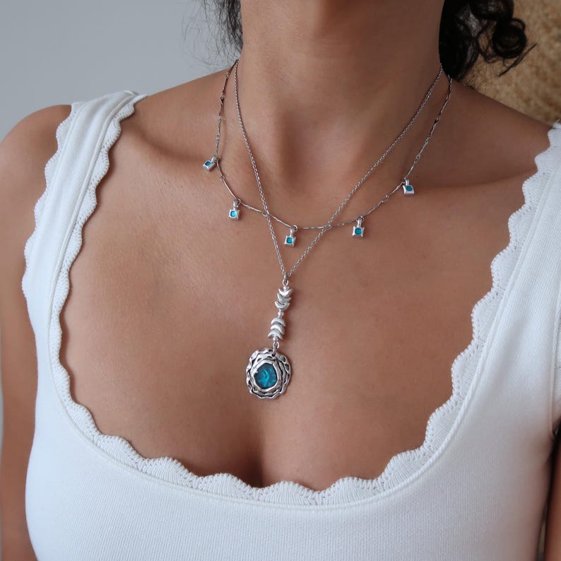 May include: A silver necklace with a turquoise pendant and a delicate chain with small turquoise stones. The pendant features a circular design with a turquoise stone in the centre.