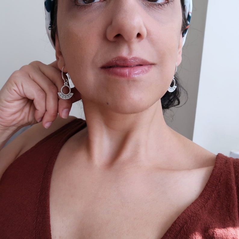 May include: A pair of silver earrings with a geometric design. The earrings are shaped like a crescent moon with a series of small, evenly spaced lines around the edge.