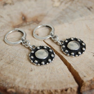 May include: A pair of silver hoop earrings with a round, textured silver charm hanging from each hoop.