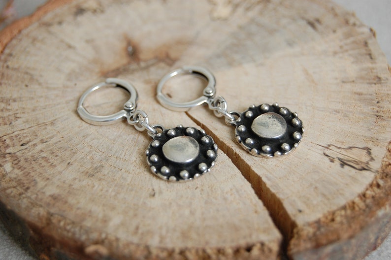 May include: A pair of silver hoop earrings with a round, textured silver charm hanging from each hoop.