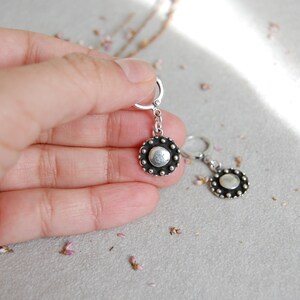 May include: A pair of silver earrings with a round, textured disc pendant. The discs have a silver center and a black outer ring with small silver dots.