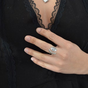 May include: A silver ring with an eye design. The ring is open and adjustable.
