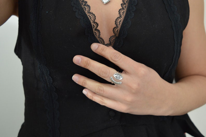May include: A silver ring with an eye design. The ring is open and adjustable.