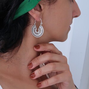 Puede incluir: Pendientes de aro plateados con un dise&ntilde;o calado detallado. Los pendientes tienen forma de semic&iacute;rculo con patrones intrincados, creando una apariencia delicada y ornamental. El dise&ntilde;o recuerda motivos florales o geom&eacute;tricos.