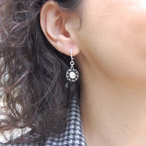 May include: Silver dangle earrings with a round, textured, silver disc with a smaller, smooth, silver circle in the center.