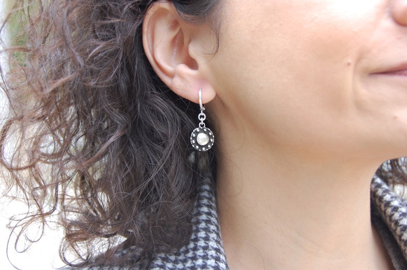 May include: Silver dangle earrings with a round, textured, silver disc with a smaller, smooth, silver circle in the center.